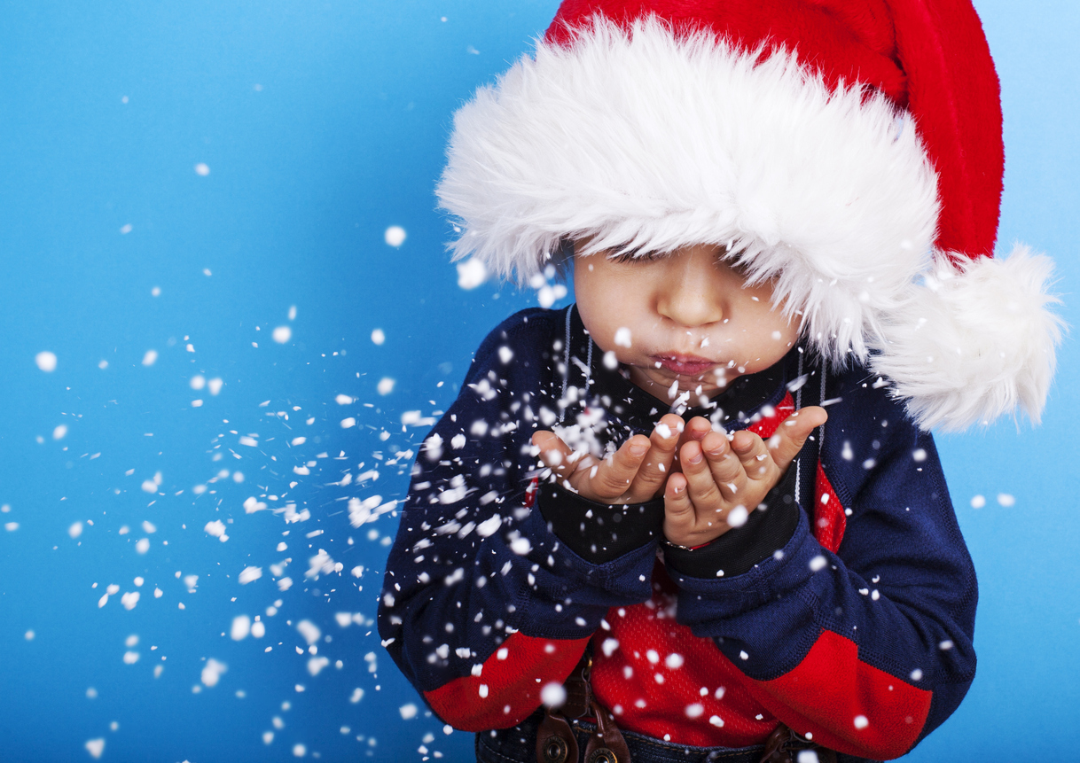 Boy in santa claus hat blowing snowflakes